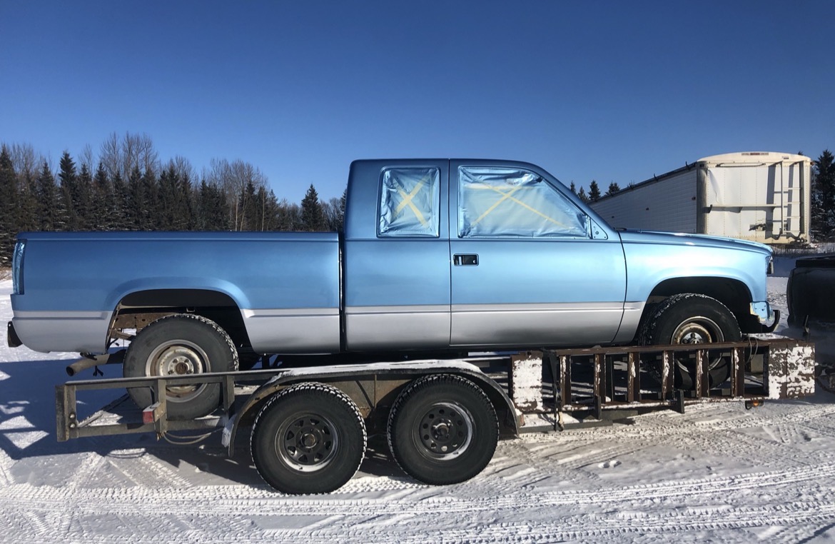 A two-tone blue pickup masked and loaded on the trailer in winter