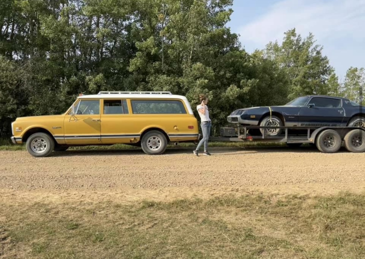 Hauling a classic car on a trailer along a gravel road