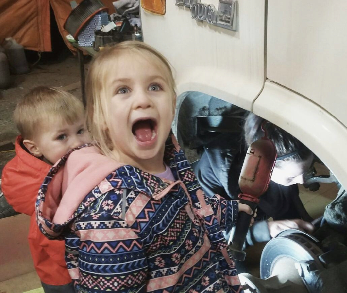 One of the kids holding the trouble light, little brother alongside, while work goes on in the van